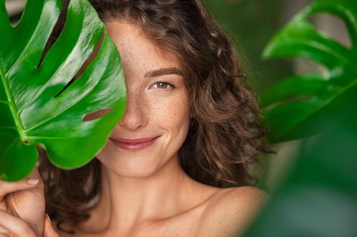 Woman with natural makeup hiding behind a leaf